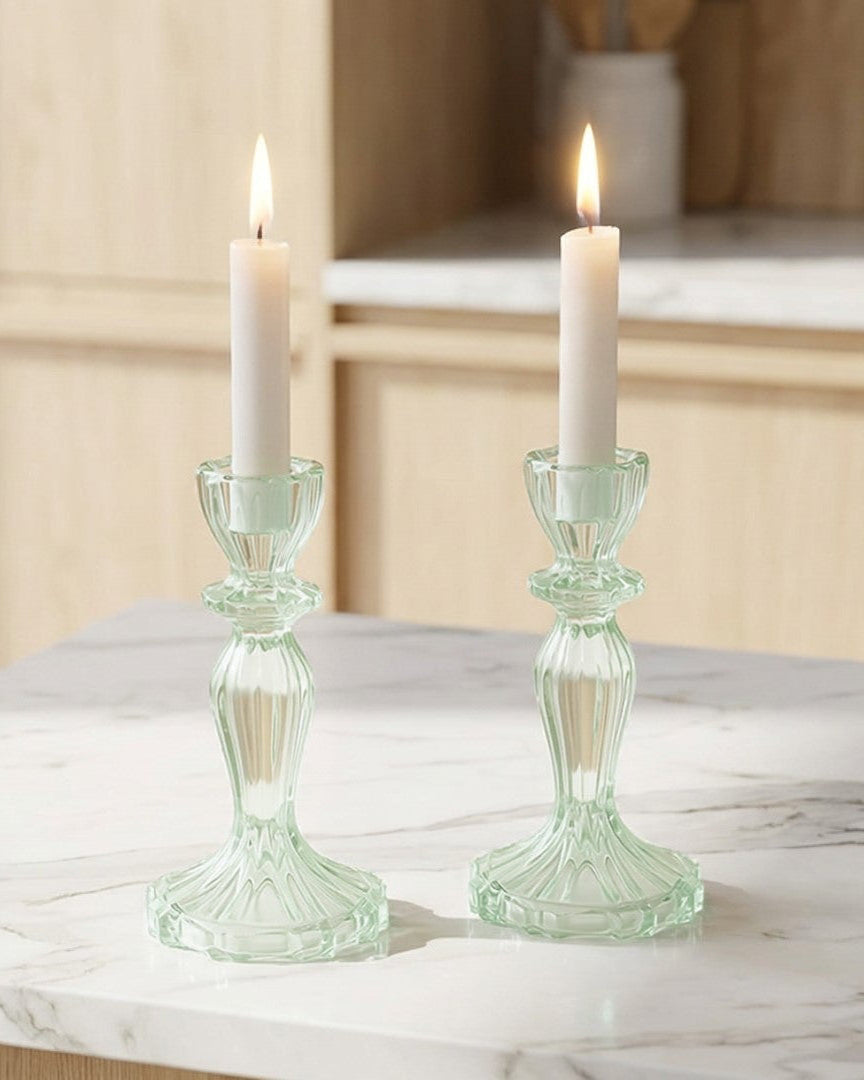 Two lit candles in green candlesticks on a marble surface with a kitchen background.