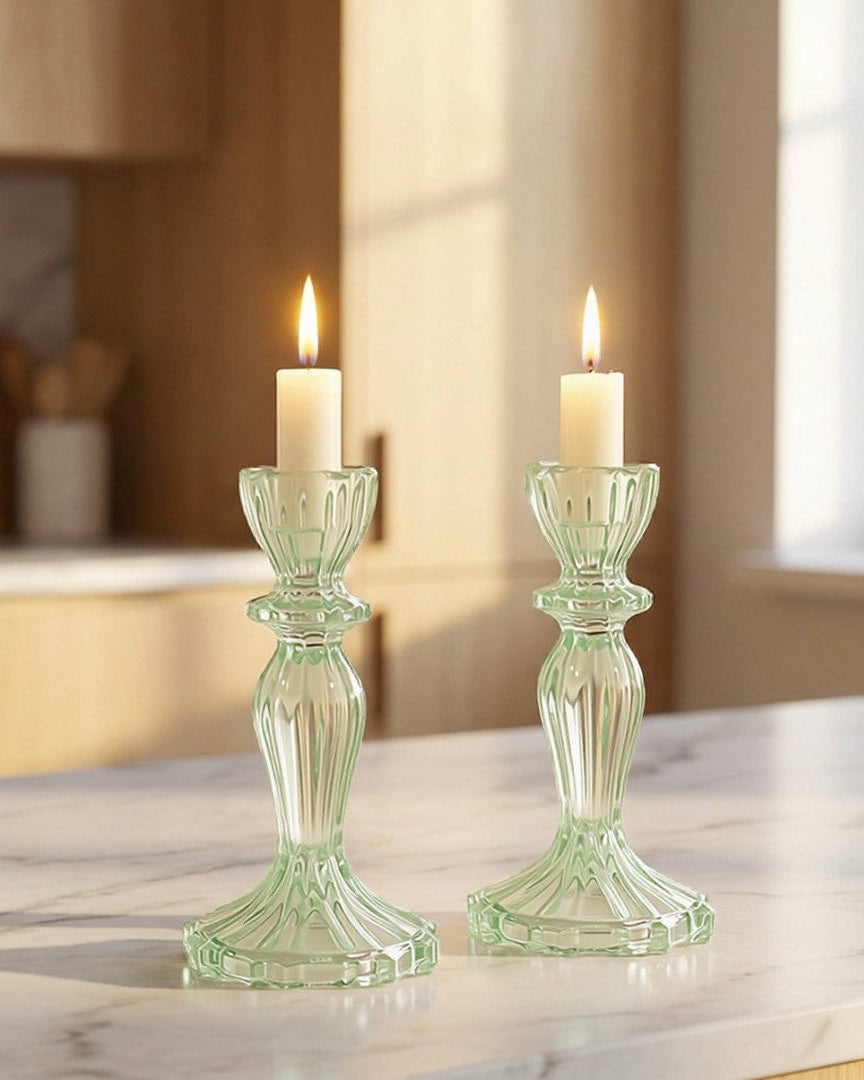 Two green candlesticks with candles on a marble countertop in a kitchen.