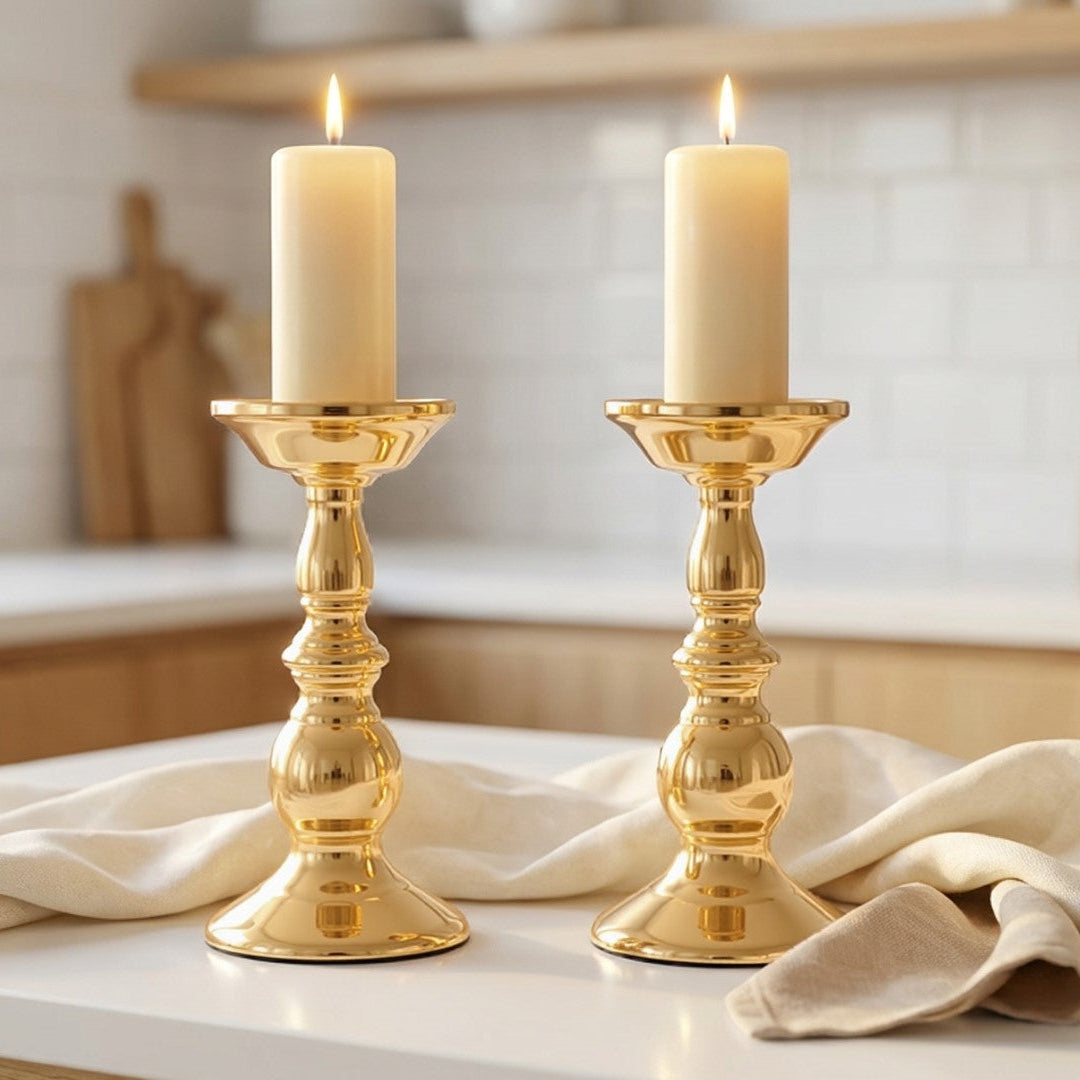 Two gold candle holders with white candles on a kitchen counter.