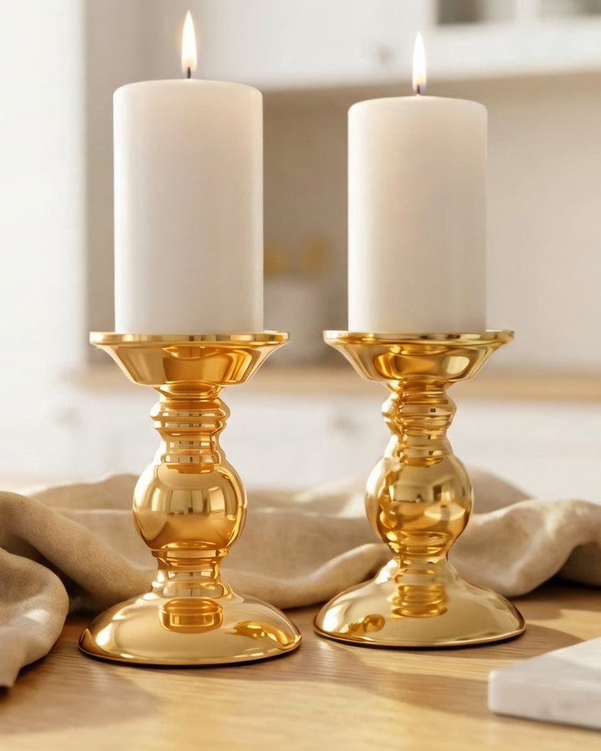 Two gold candle holders with white candles on a wooden surface.