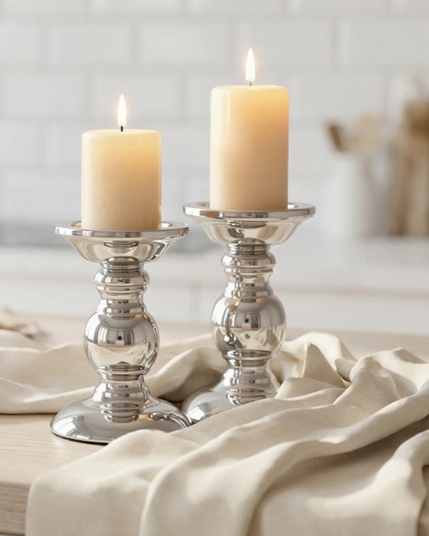 Two candles in silver candle holders on a wooden surface with a white towel.