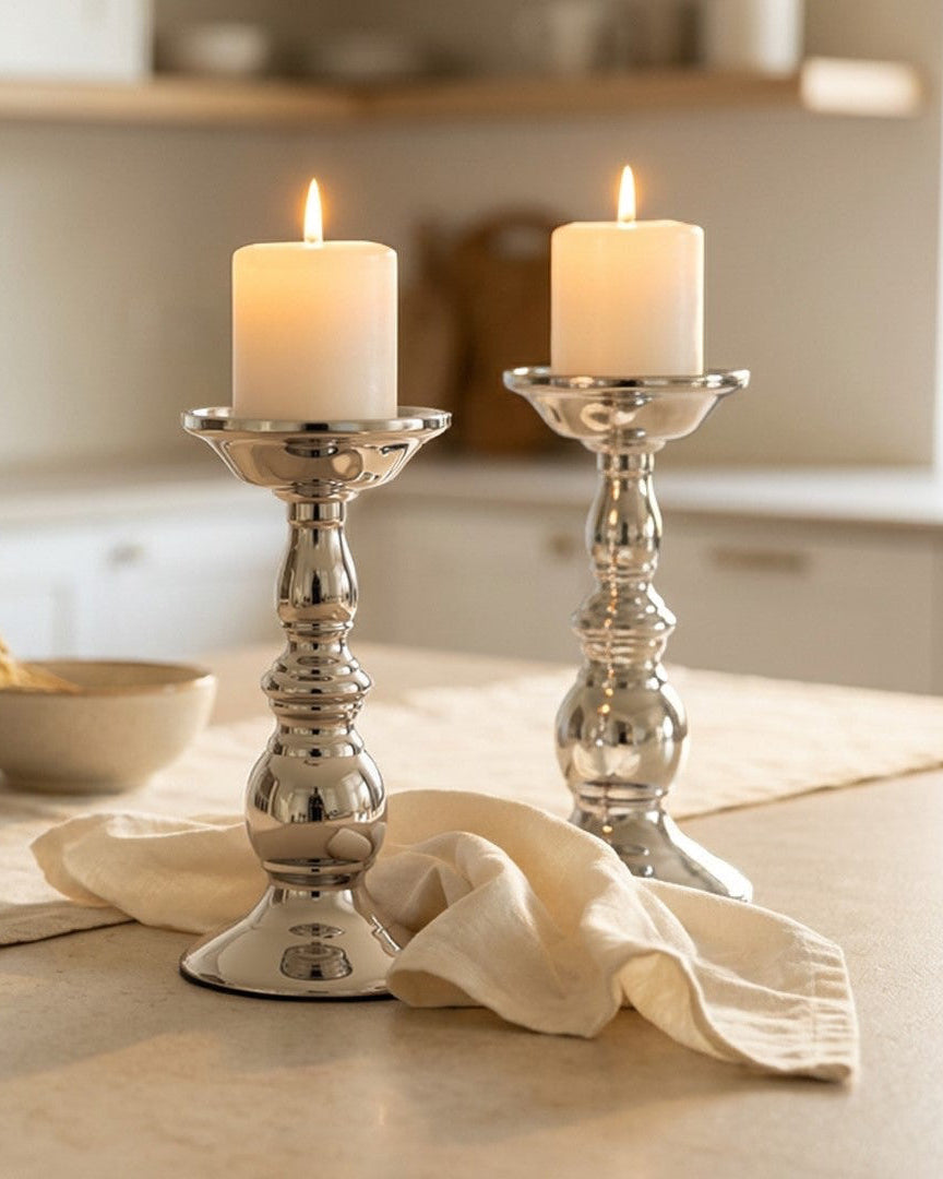Two silver candle holders with lit candles on a kitchen counter.