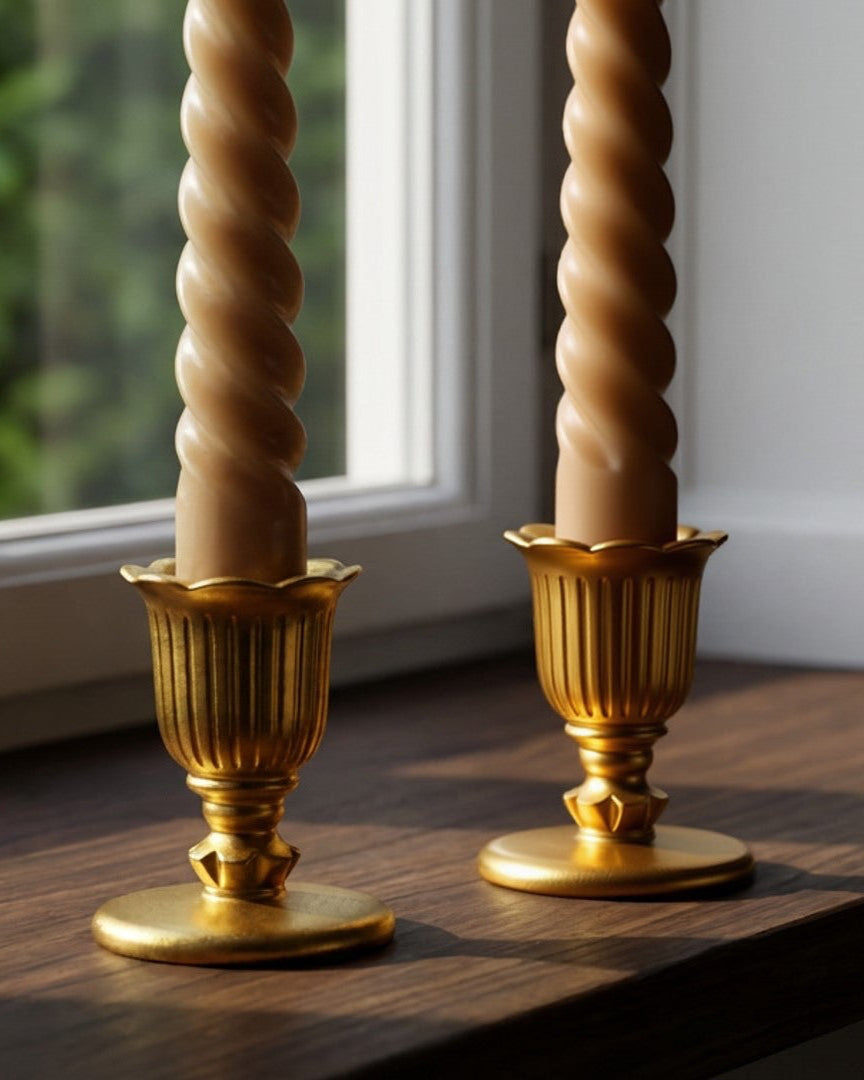 Two gold candle holders with spiral candles on a windowsill.