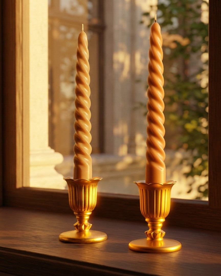 Two gold candle holders with twisted candles on a windowsill with sunlight casting shadows.