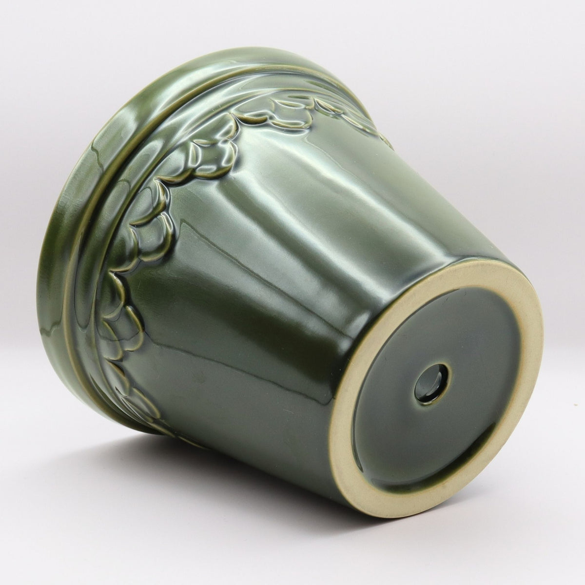 Green ceramic pot with decorative patterns and eucalyptus leaves on a white background