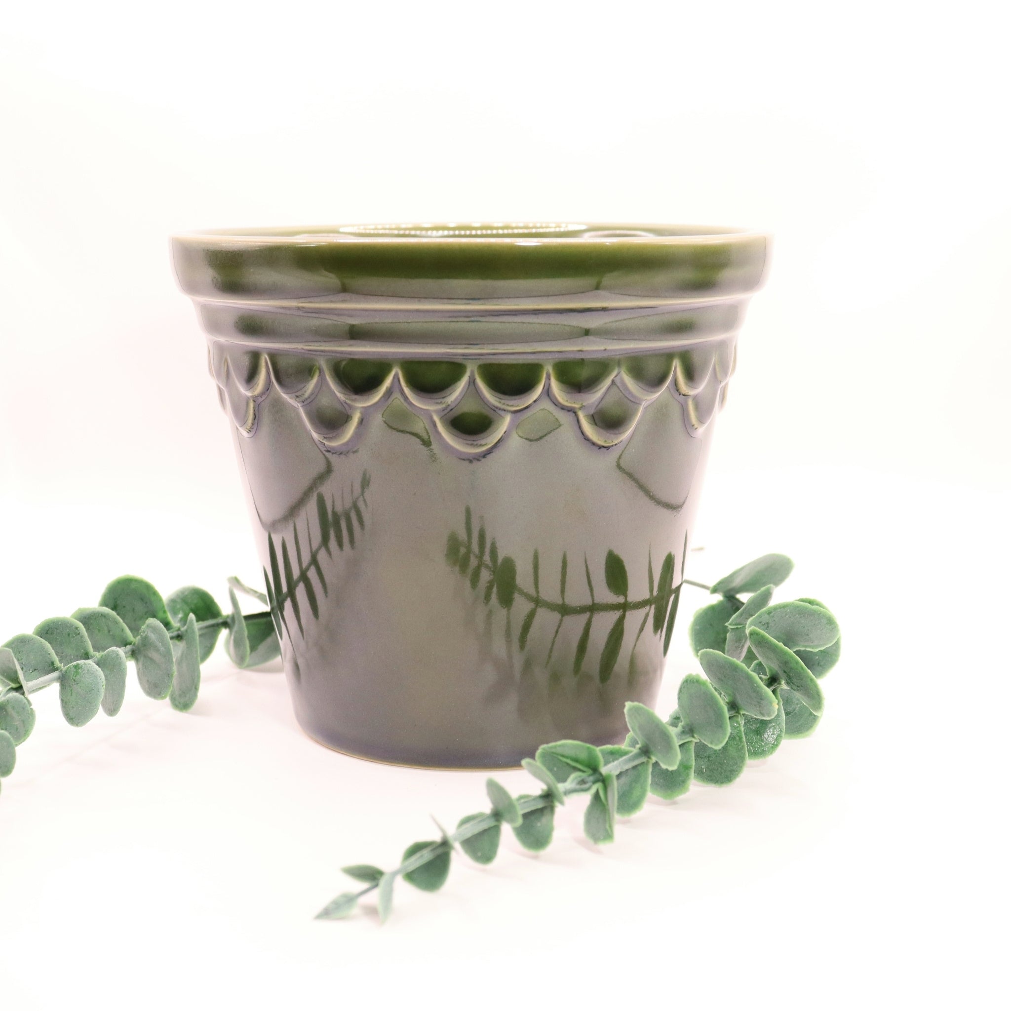 Green ceramic pot with decorative patterns and eucalyptus leaves on a white background