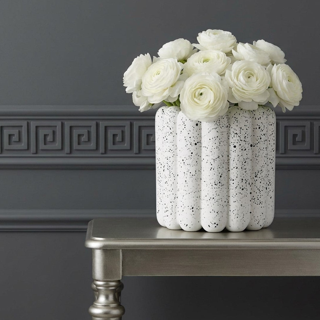 White vase with flowers on a silver table against a dark gray wall with decorative molding.