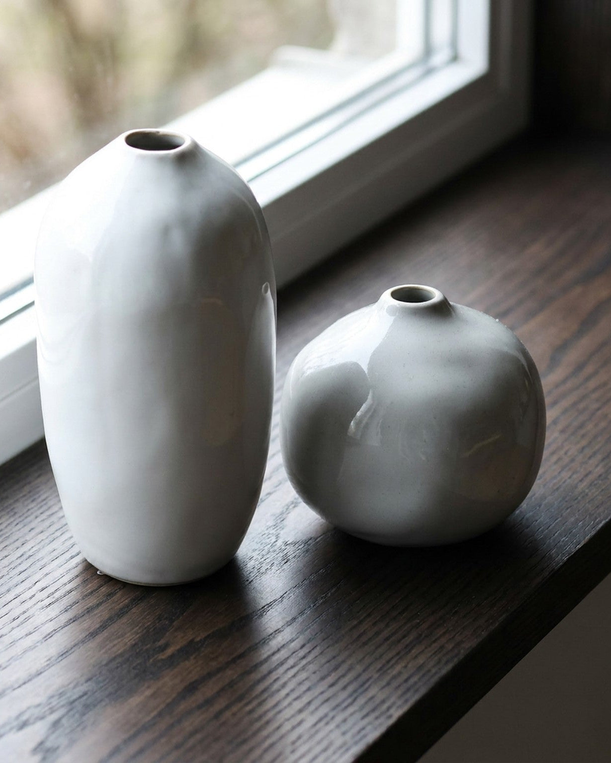 Two ceramic vases on a wooden surface with a window in the background