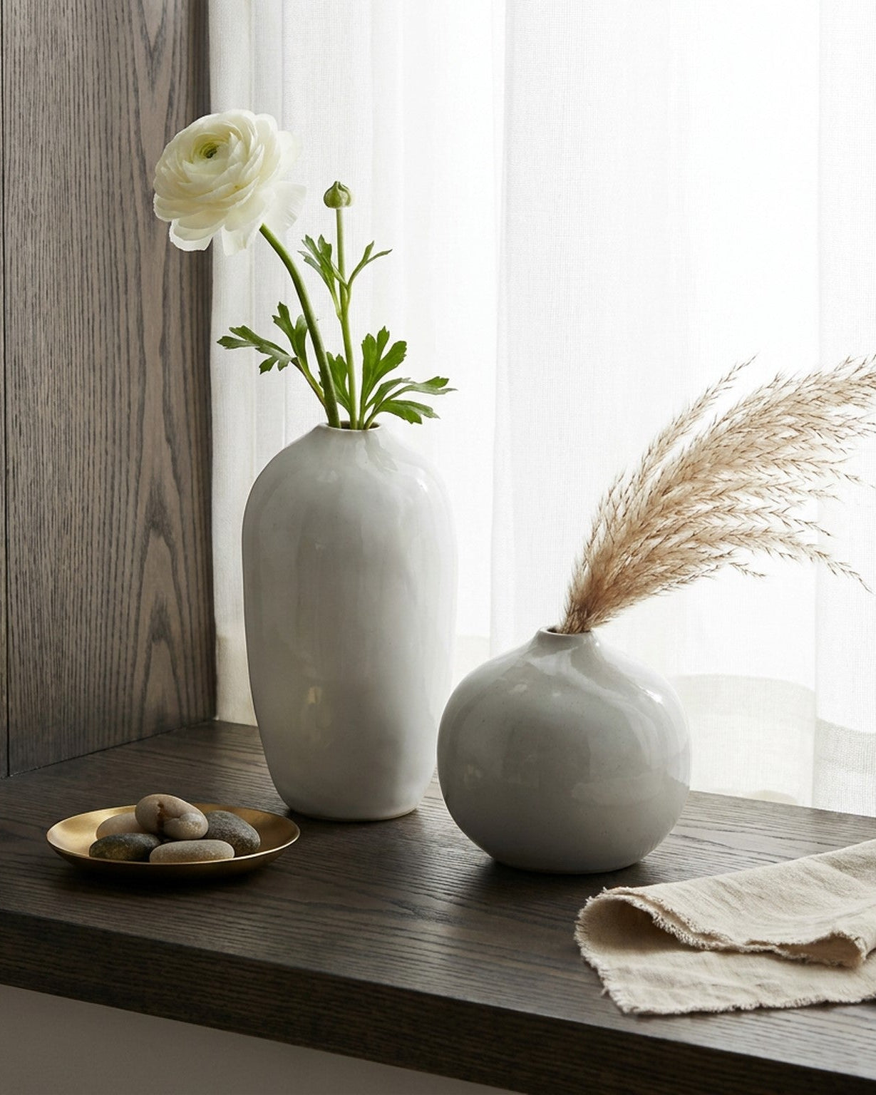 Two white vases with flowers and dried grass on a wooden surface.