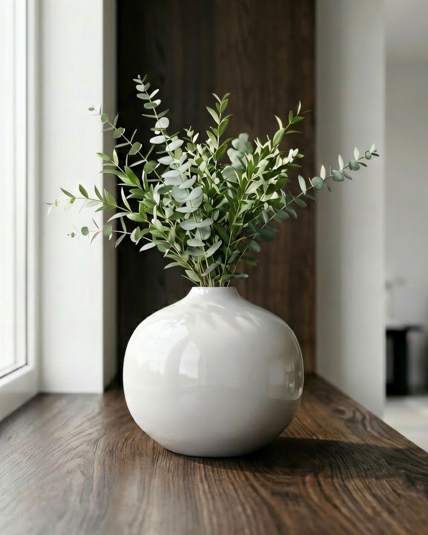 White vase with greenery on a wooden floor in a modern living room.