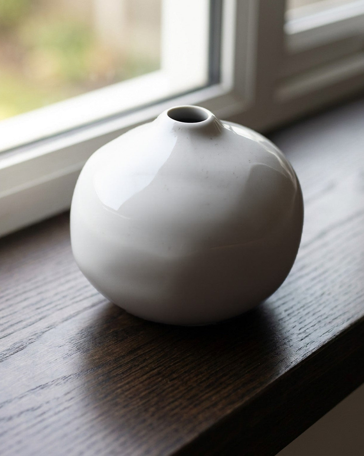 White ceramic vase on a wooden surface with a window in the background