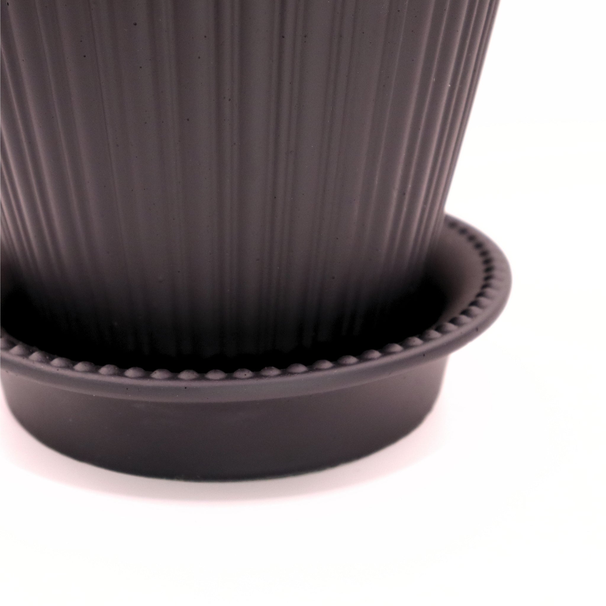 Close-up of a black ribbed pot with matching saucer on a white background