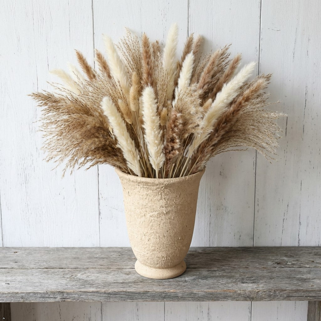 Woven vase with dried pampas grass on a wooden shelf against a white wooden wall.