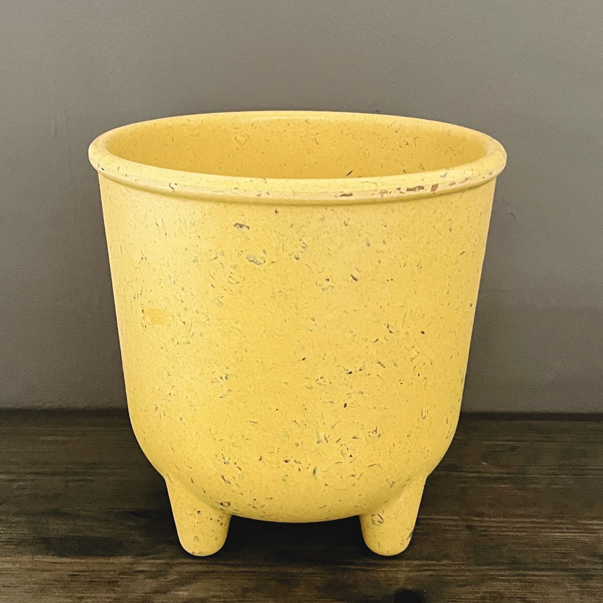 Yellow ceramic pot with textured surface on a wooden surface against a gray wall.