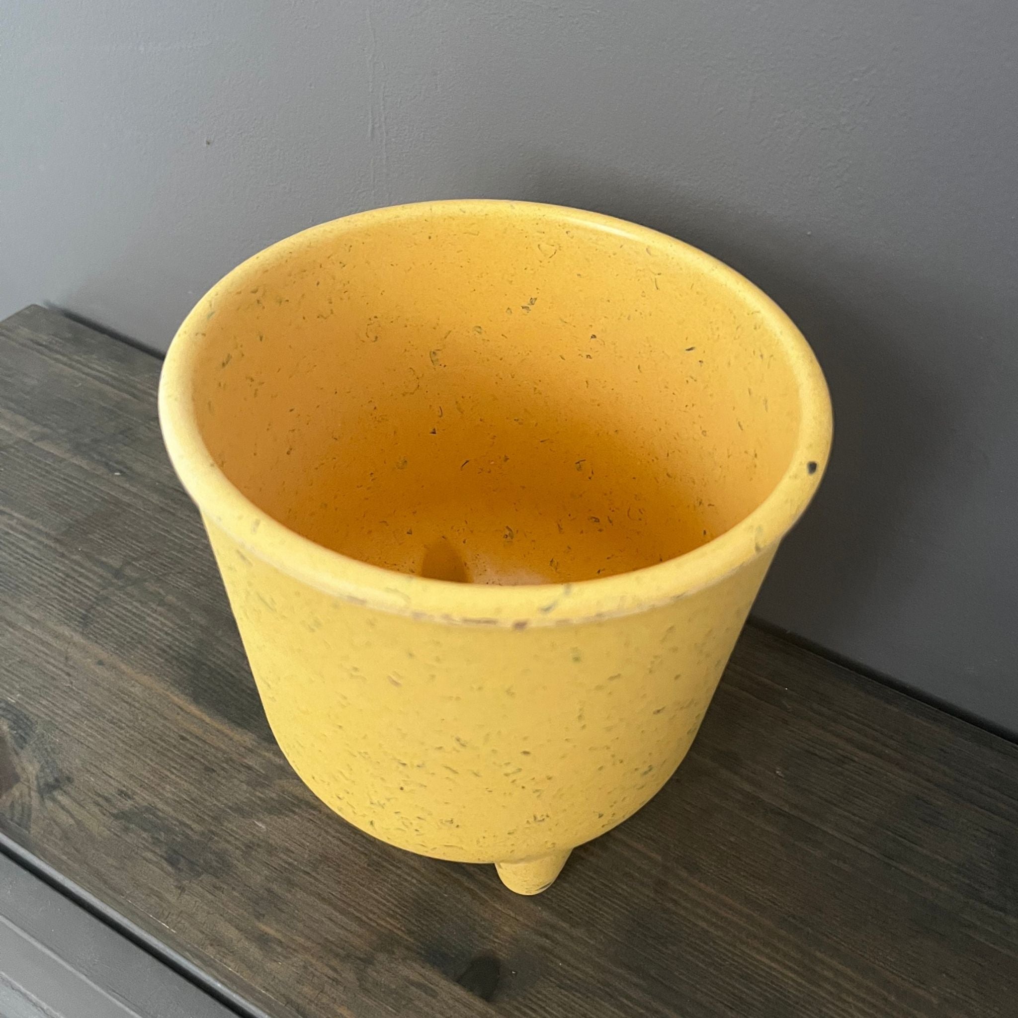 Yellow ceramic pot on a wooden surface with a gray wall background