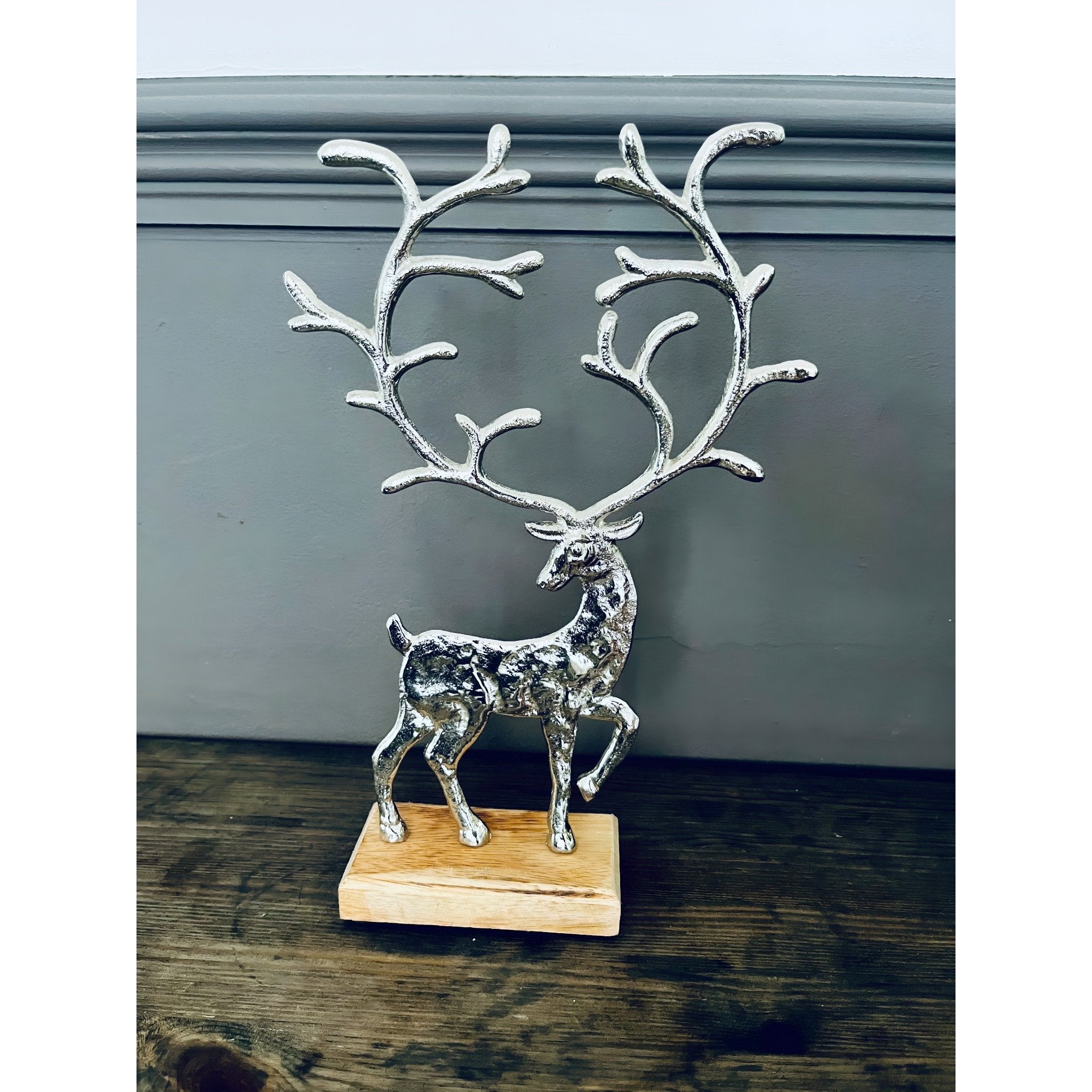 Decorative silver deer figurine with large antlers on a wooden base against a plain background