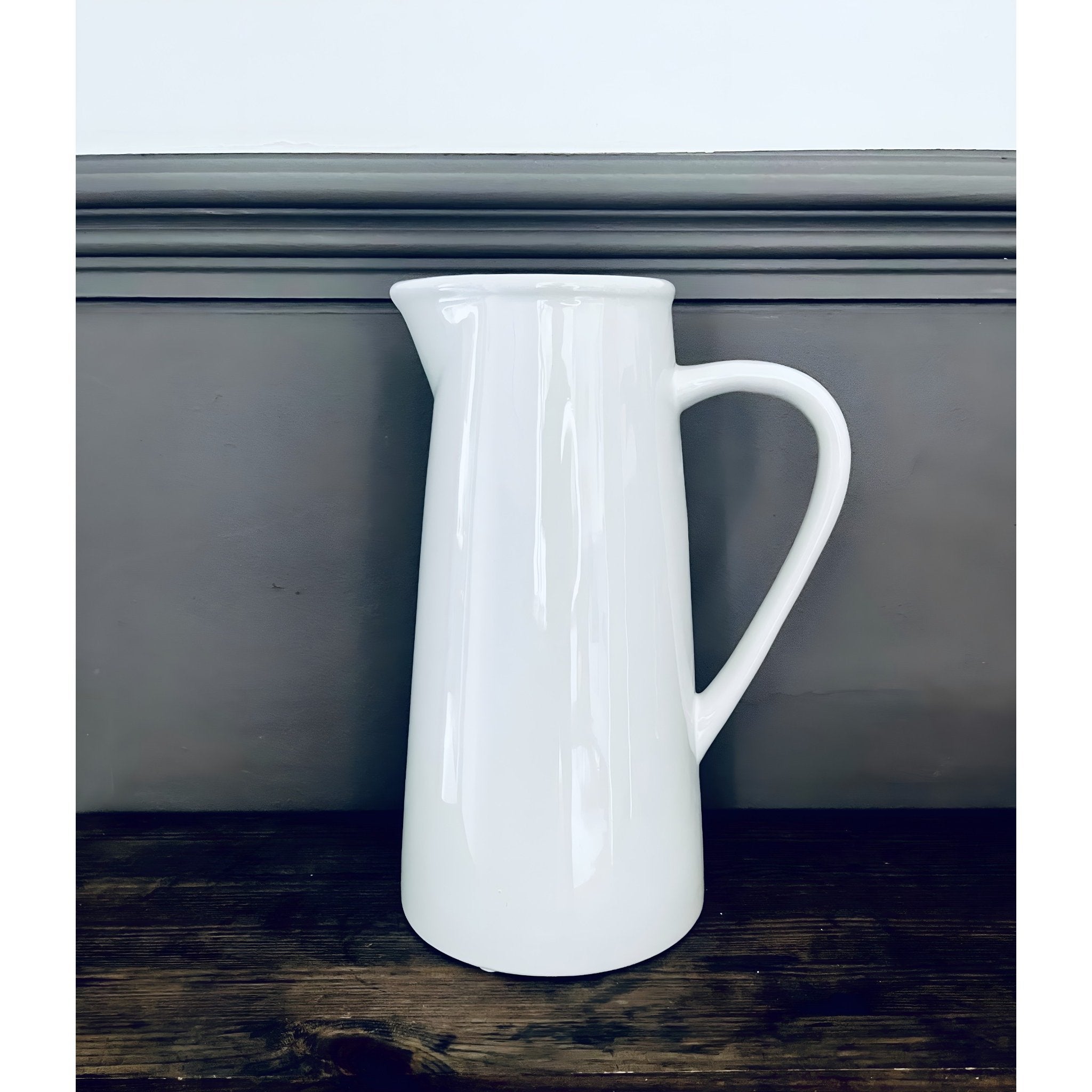 White ceramic pitcher on a wooden surface with a neutral background