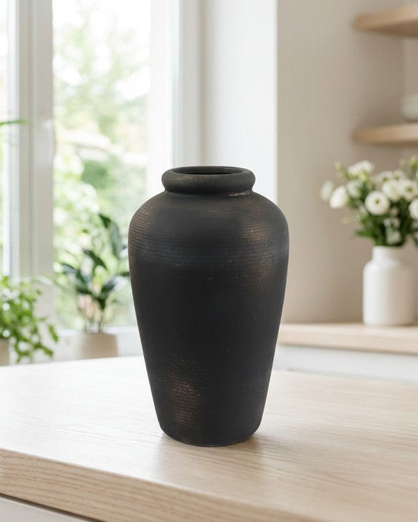Black vase on a wooden surface with a blurred indoor background