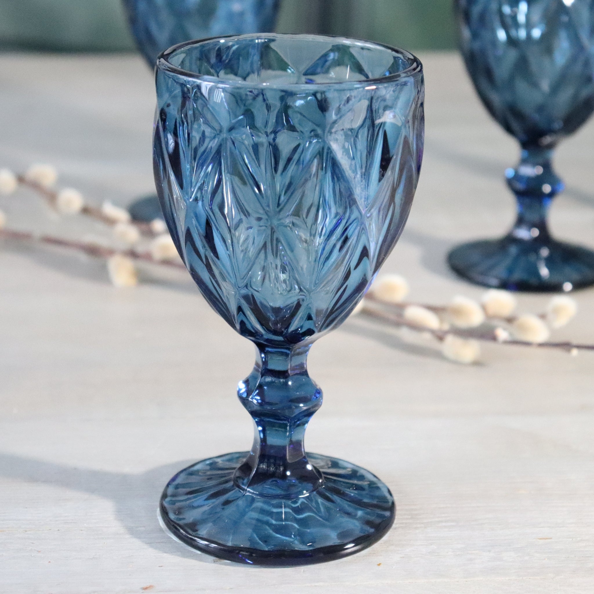 Luxury blue glass wine goblet with intricate patterns on a light wooden surface.