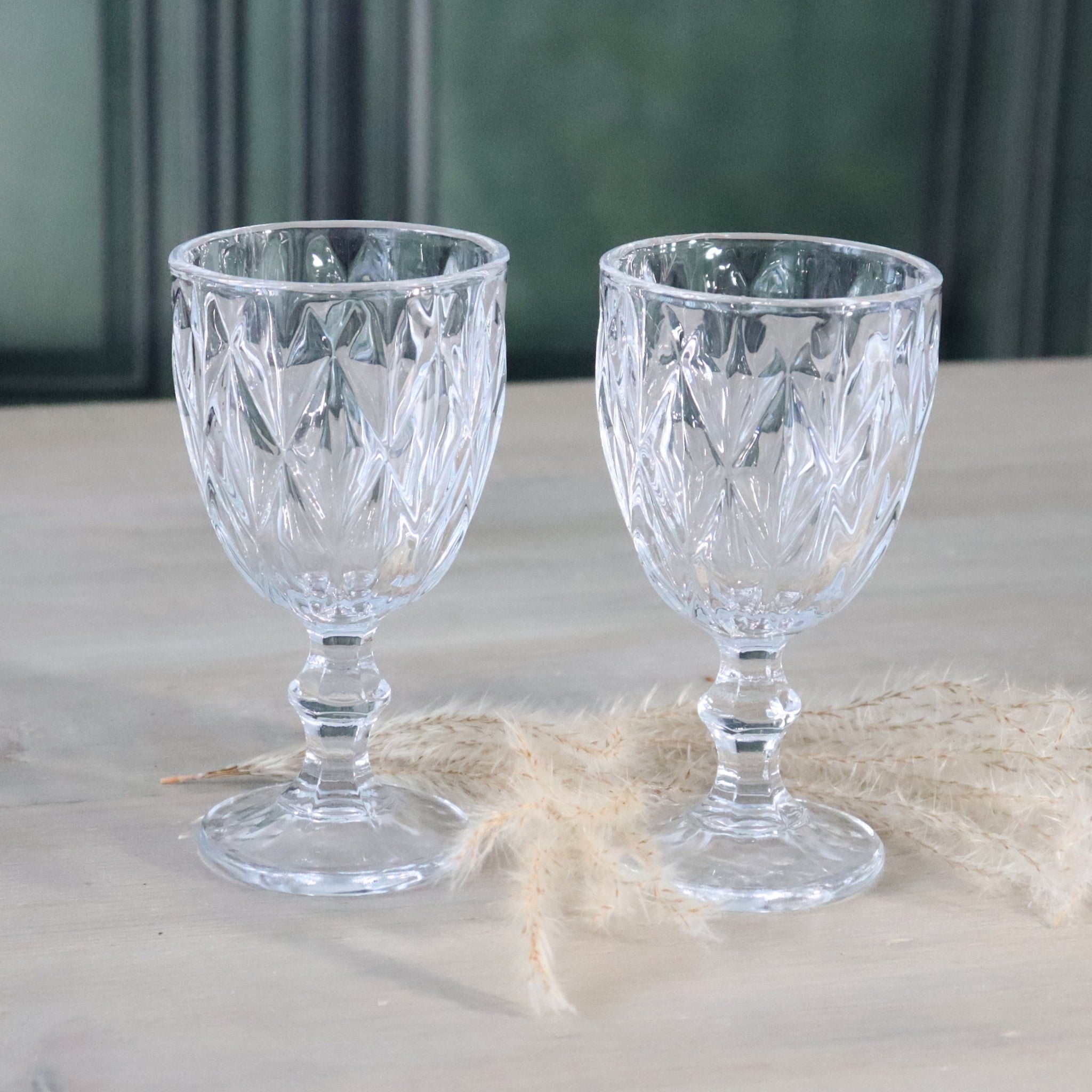 Two clear glass goblets with intricate patterns on a light surface.