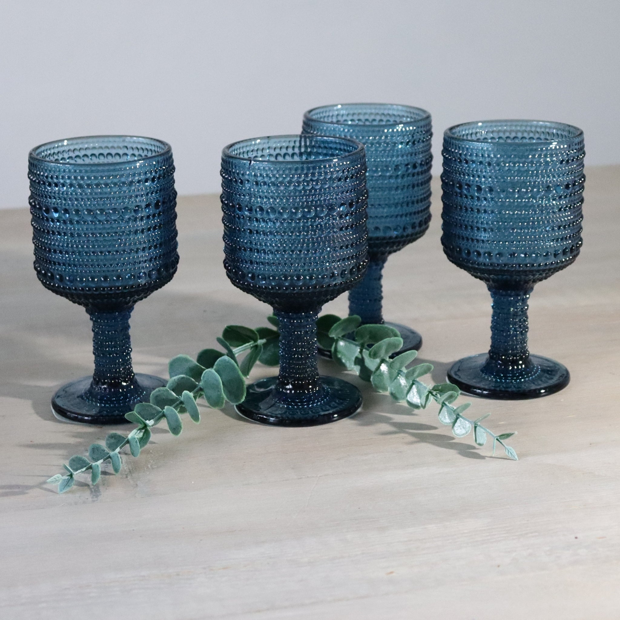 4 blue textured wine goblets on wooden white surface