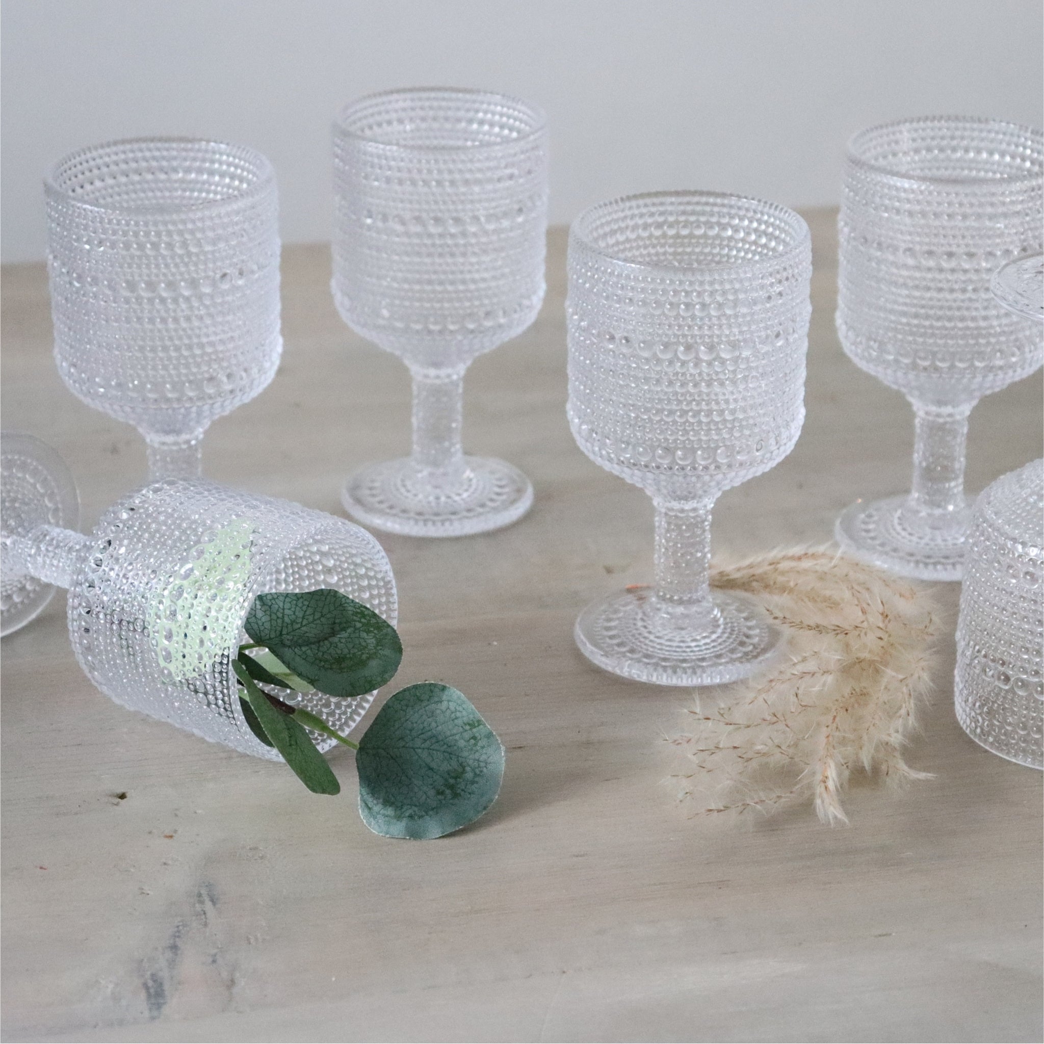 5 clear textured wine goblets on wooden white surface