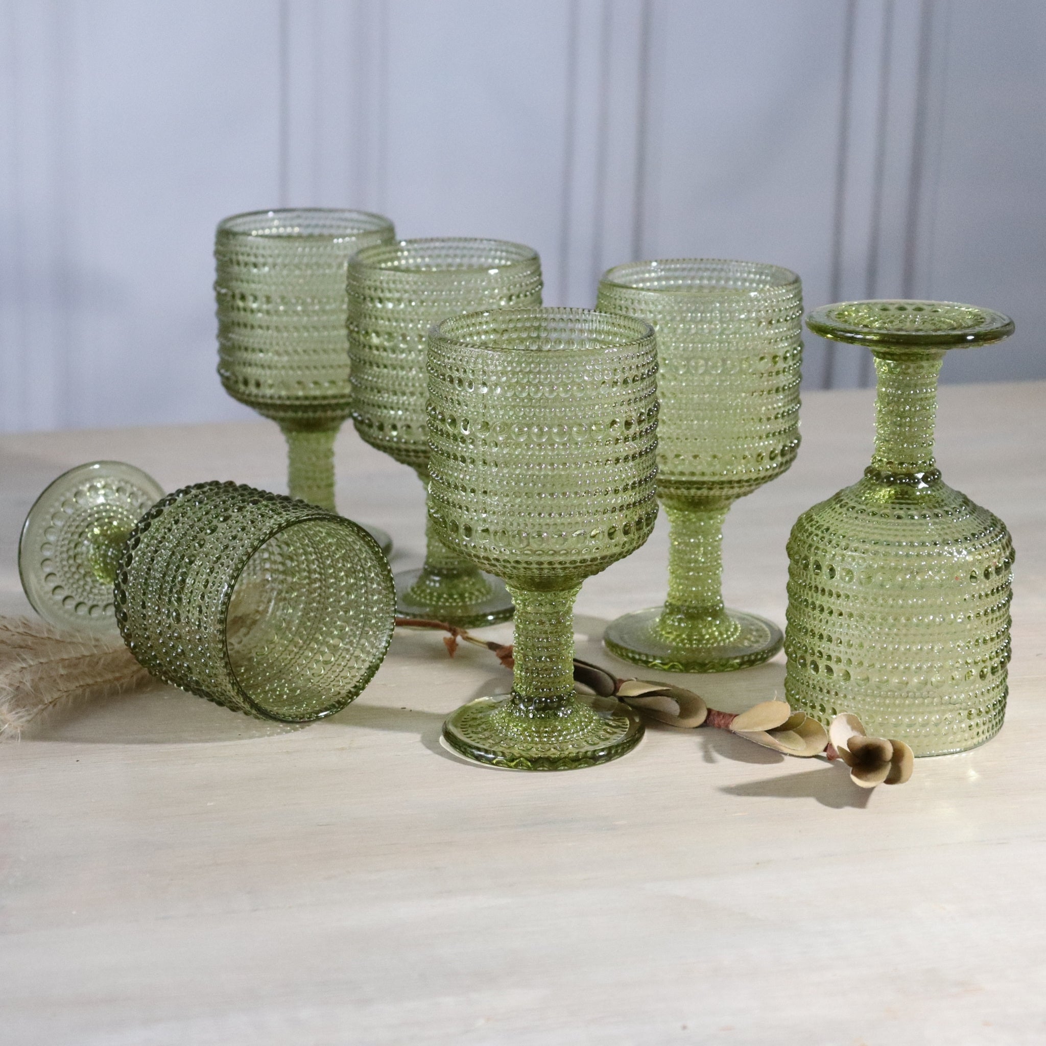 Set of green textured glass goblets on a light surface with a neutral background
