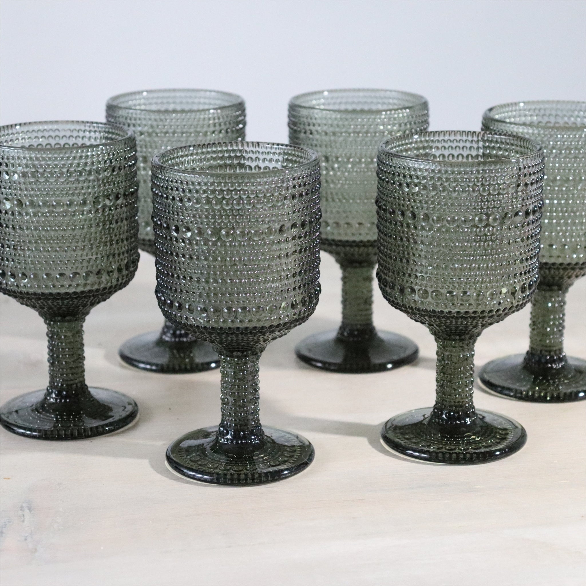 6 grey textured wine goblets on wooden white surface