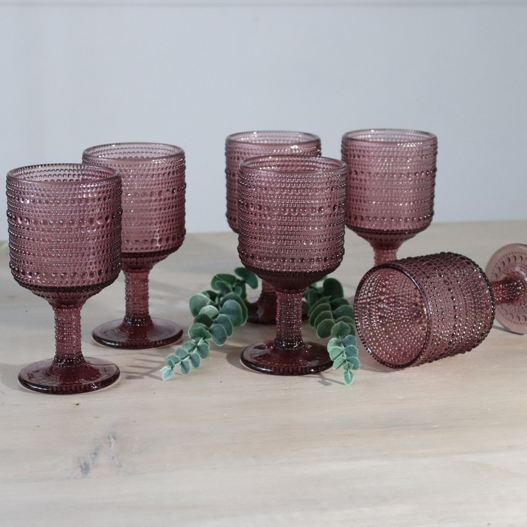 6 purple textured wine goblets on wooden white surface
