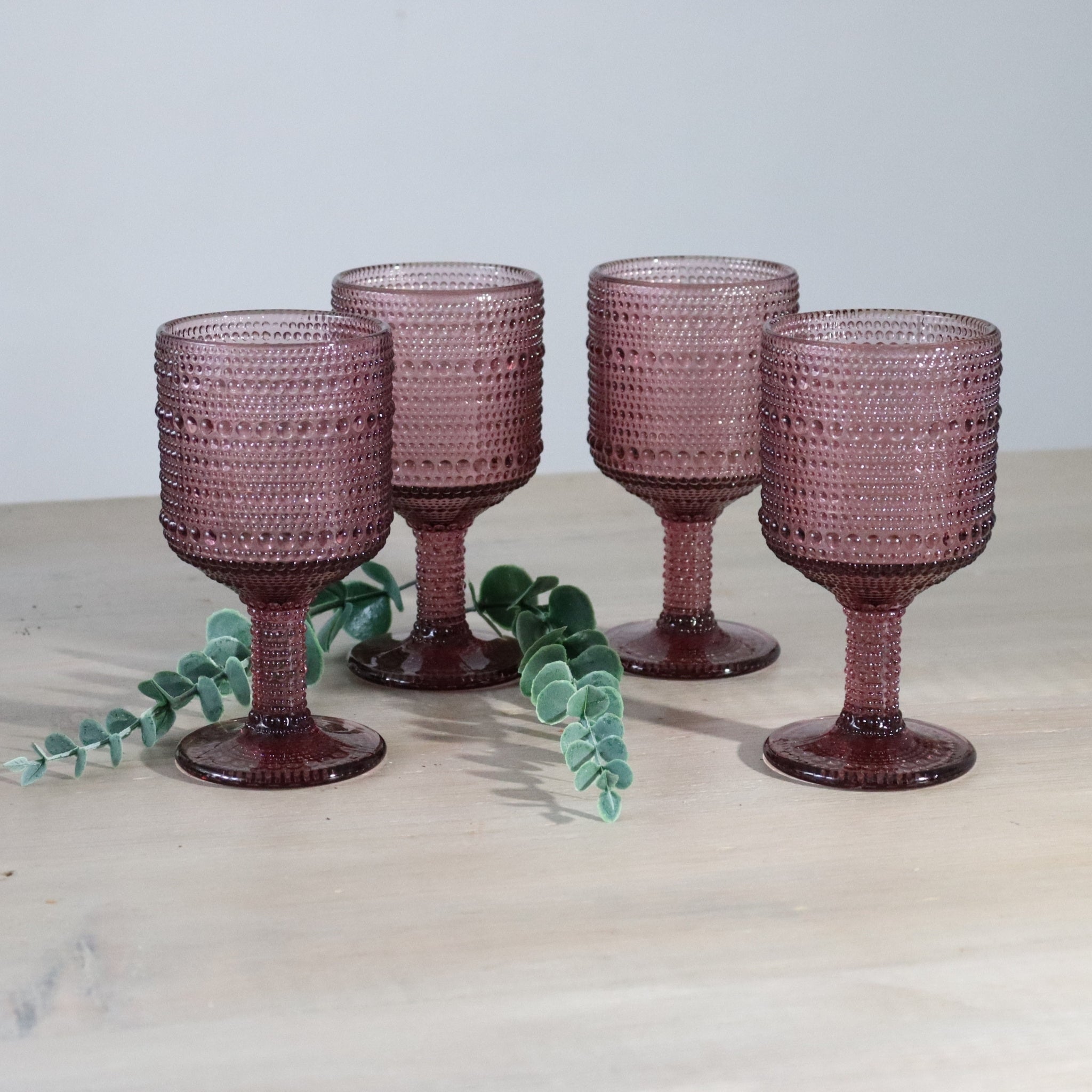 Four textured purple glasses on a light surface with a leafy branch.