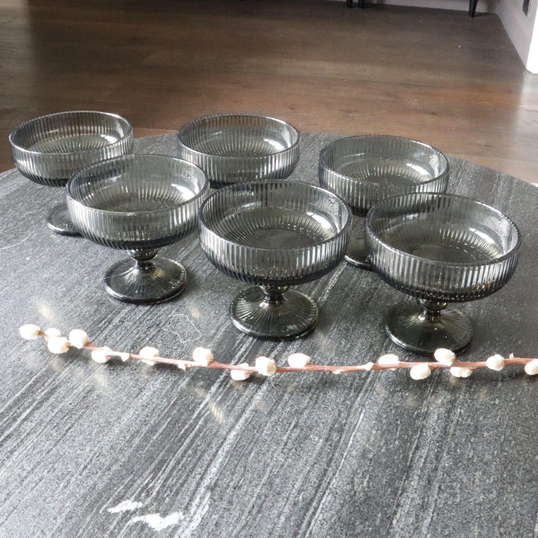 Set of six ribbed glass dessert bowls on a textured surface with a decorative branch.