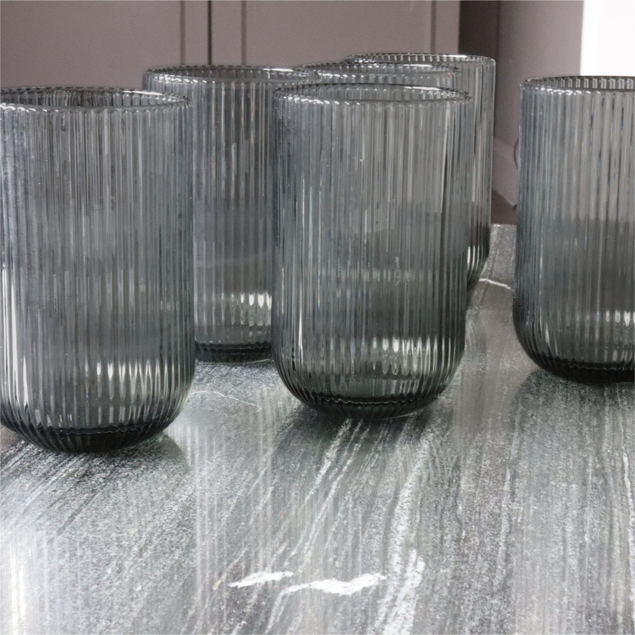 Set of ribbed glass tumblers on a reflective surface with a neutral background