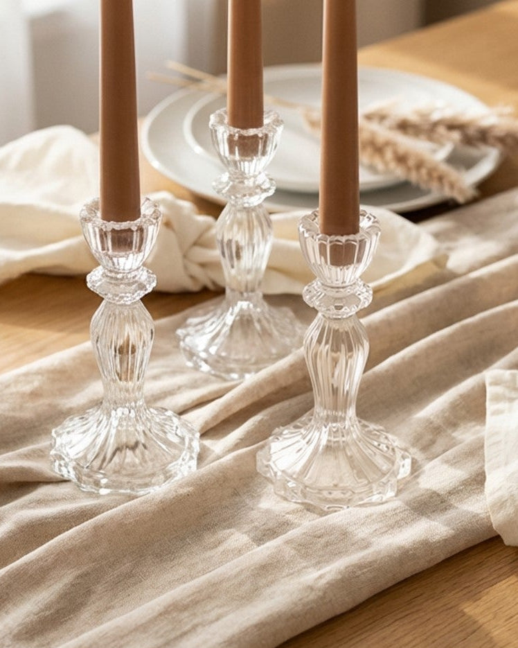 Two clear glass candle holders with candles on a textured surface