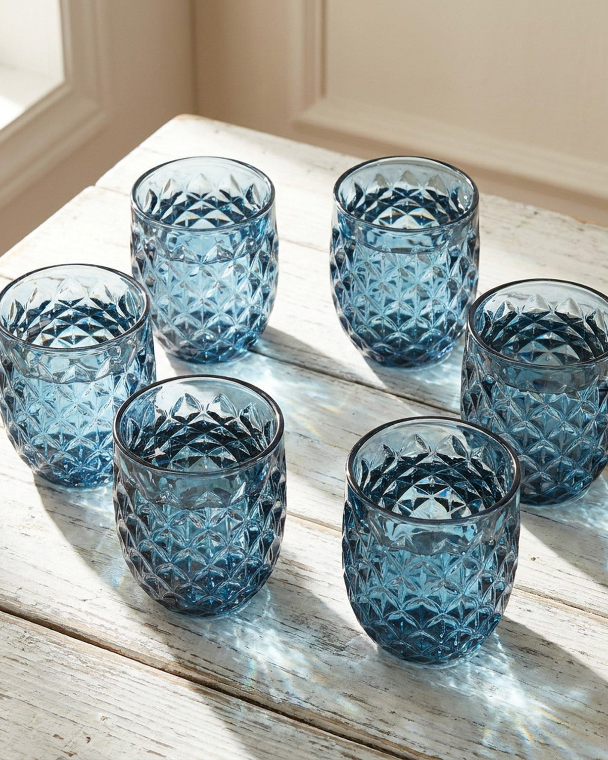 Set of blue textured glass tumblers on a light surface with greenery.