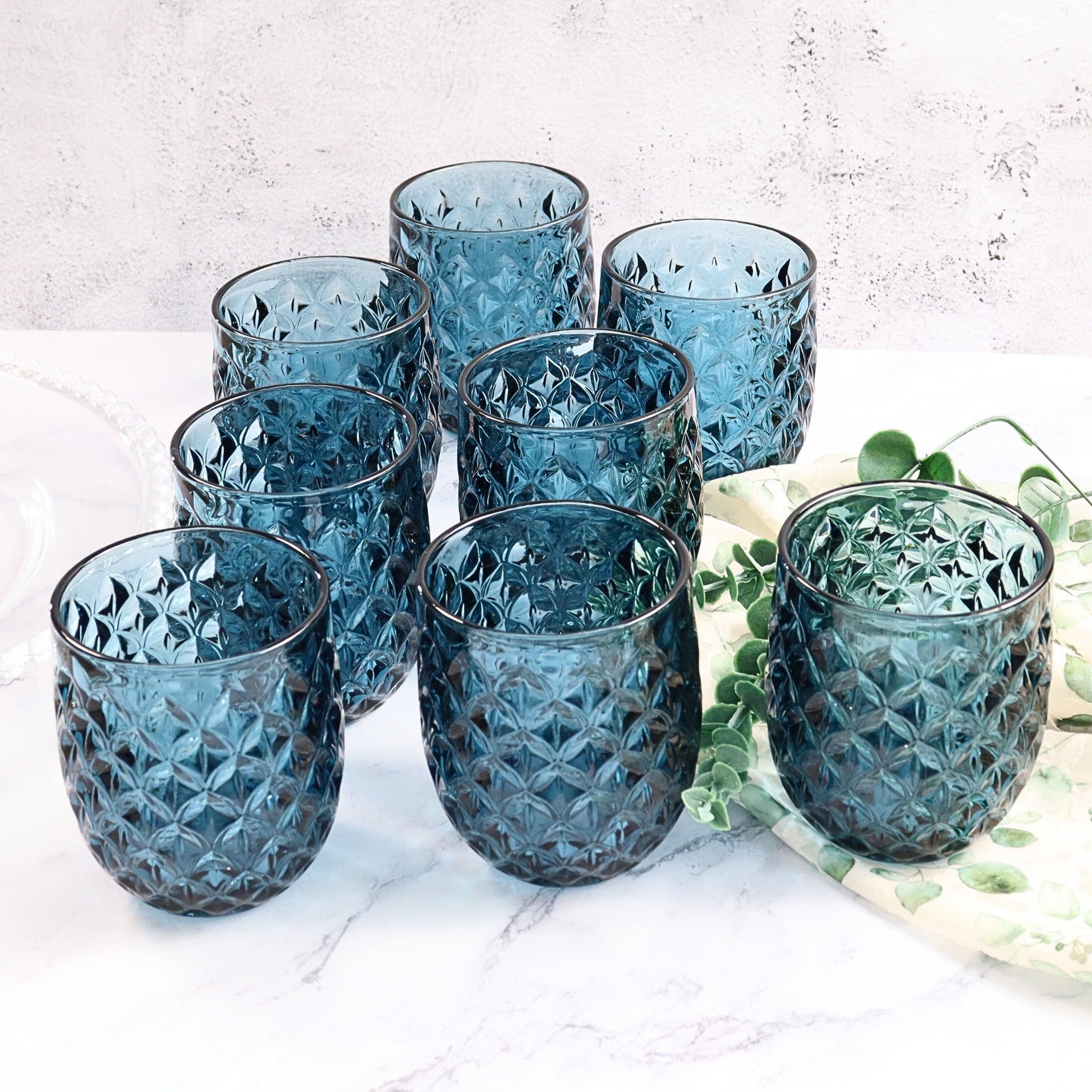 Set of blue textured glass tumblers on a light surface with greenery.