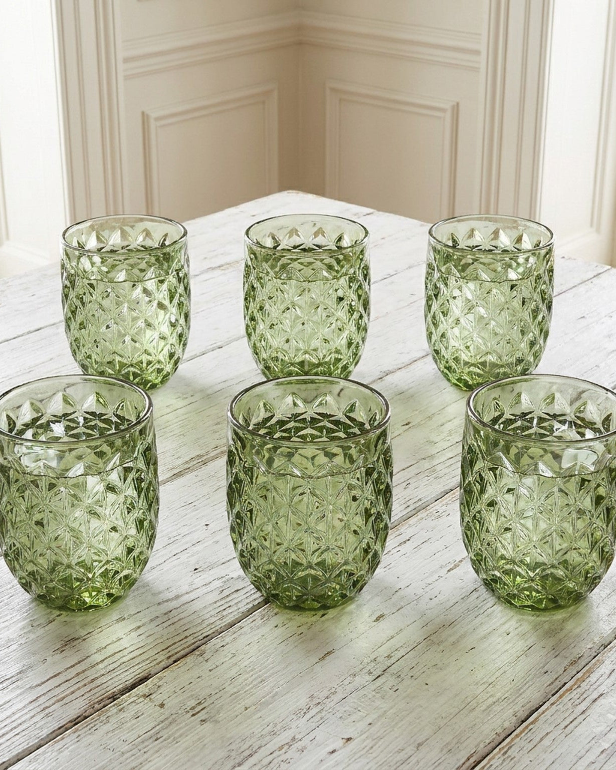 Set of green patterned glass tumblers on a white surface with a gray background
