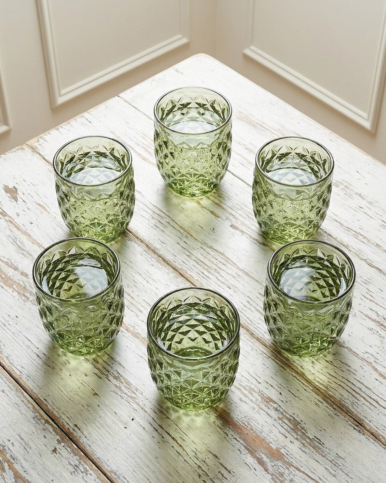 Set of four green textured glass tumblers on a marble surface with a gray background