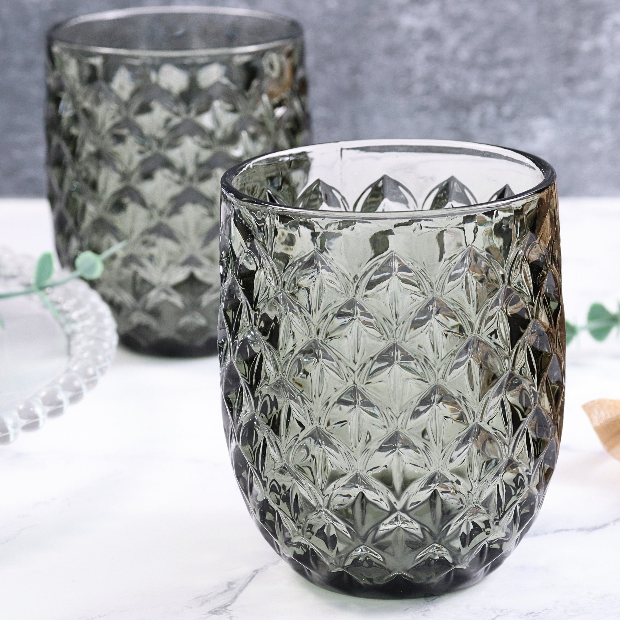Two textured glass tumblers on a light surface with a blurred background