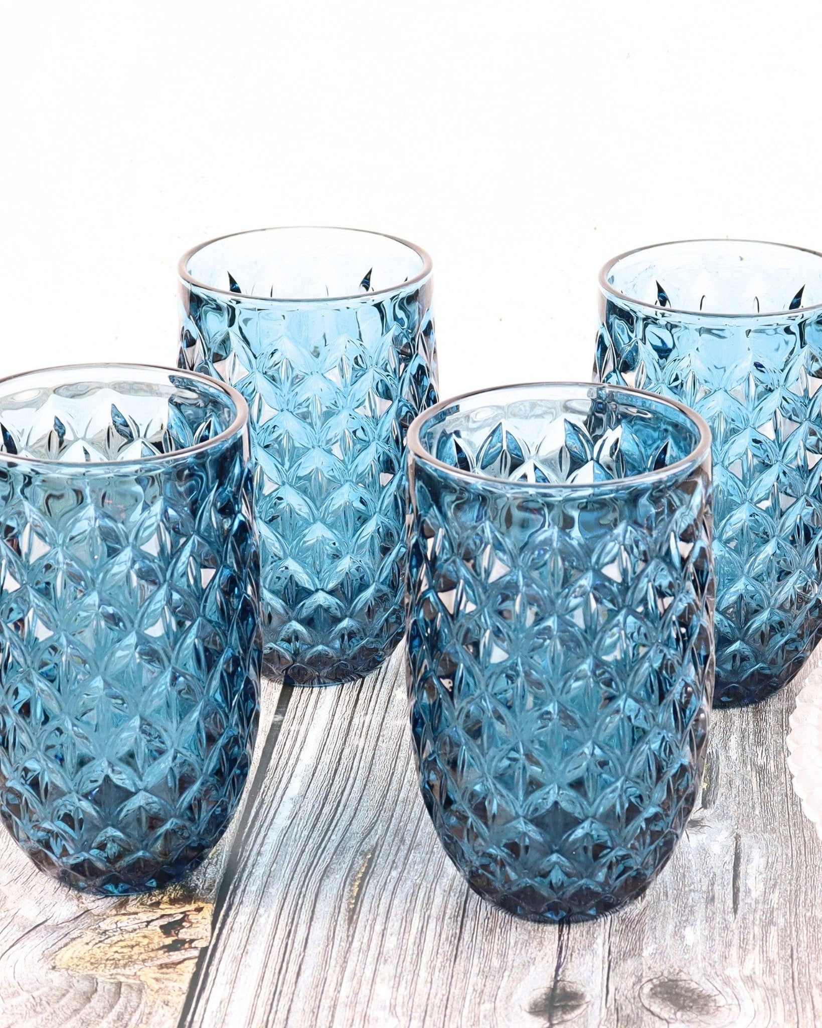 Set of four blue textured glass tumblers on a wooden surface