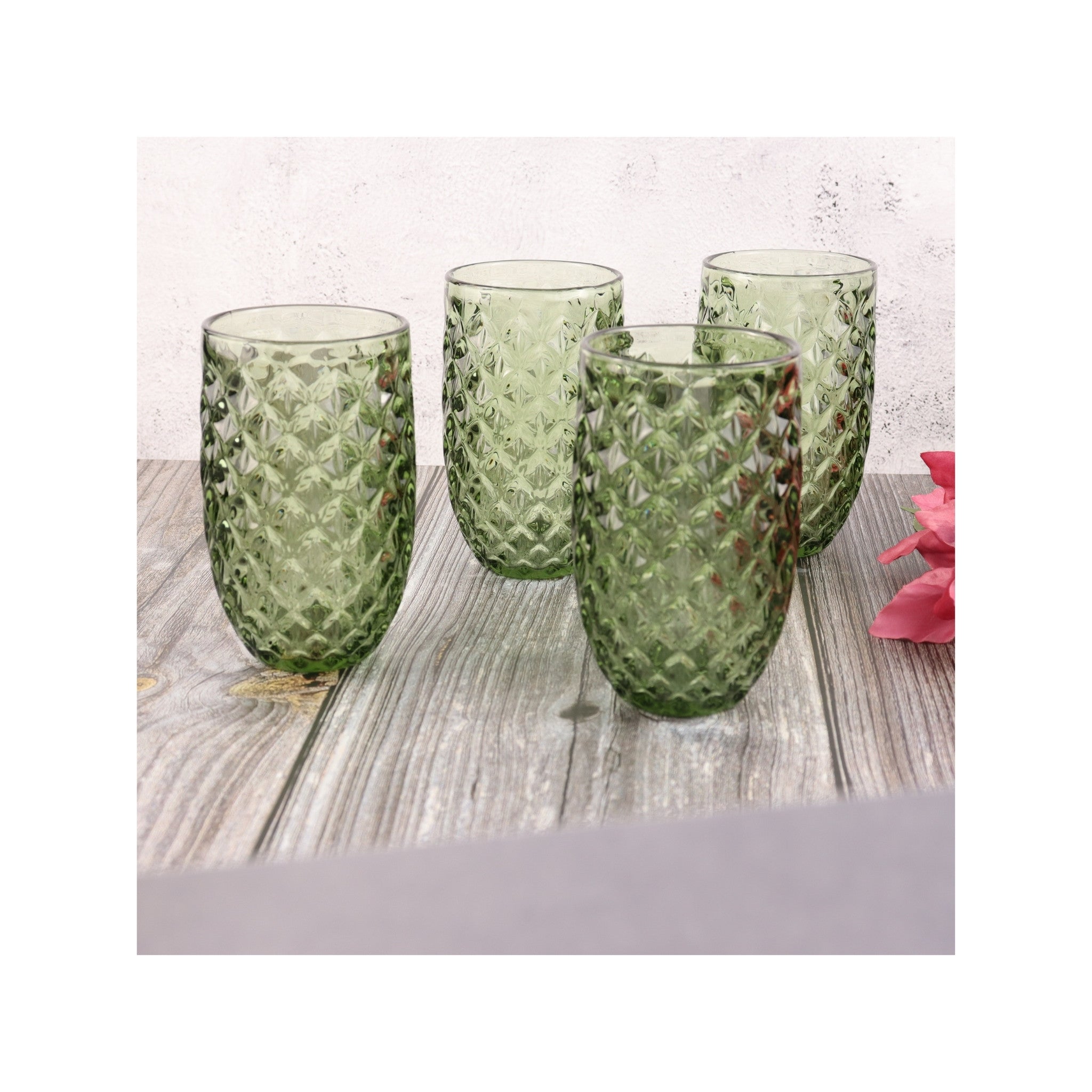 Set of four green textured glass tumblers on a wooden surface with a white background