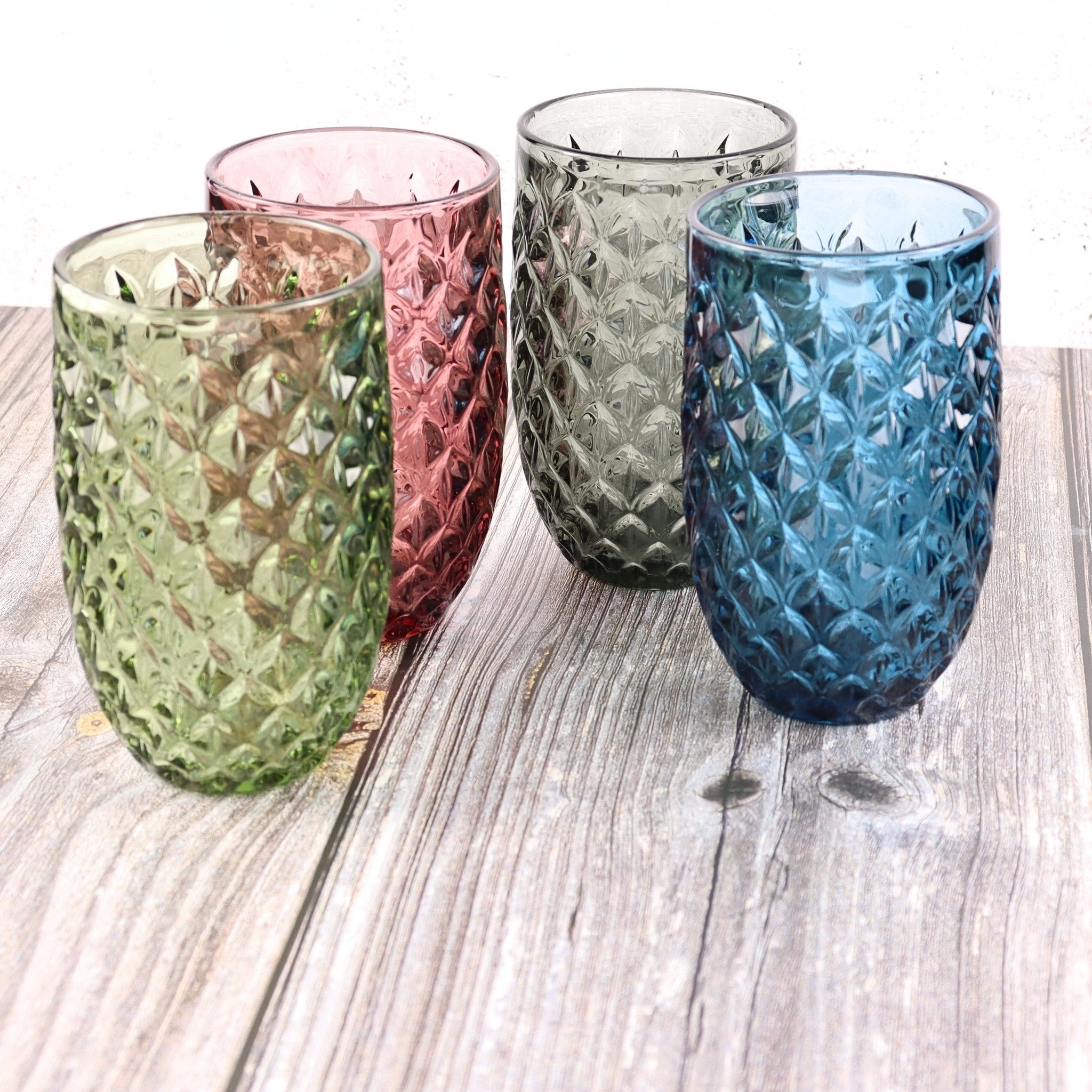 Four textured glass tumblers in green, pink, gray, and blue on a wooden surface.