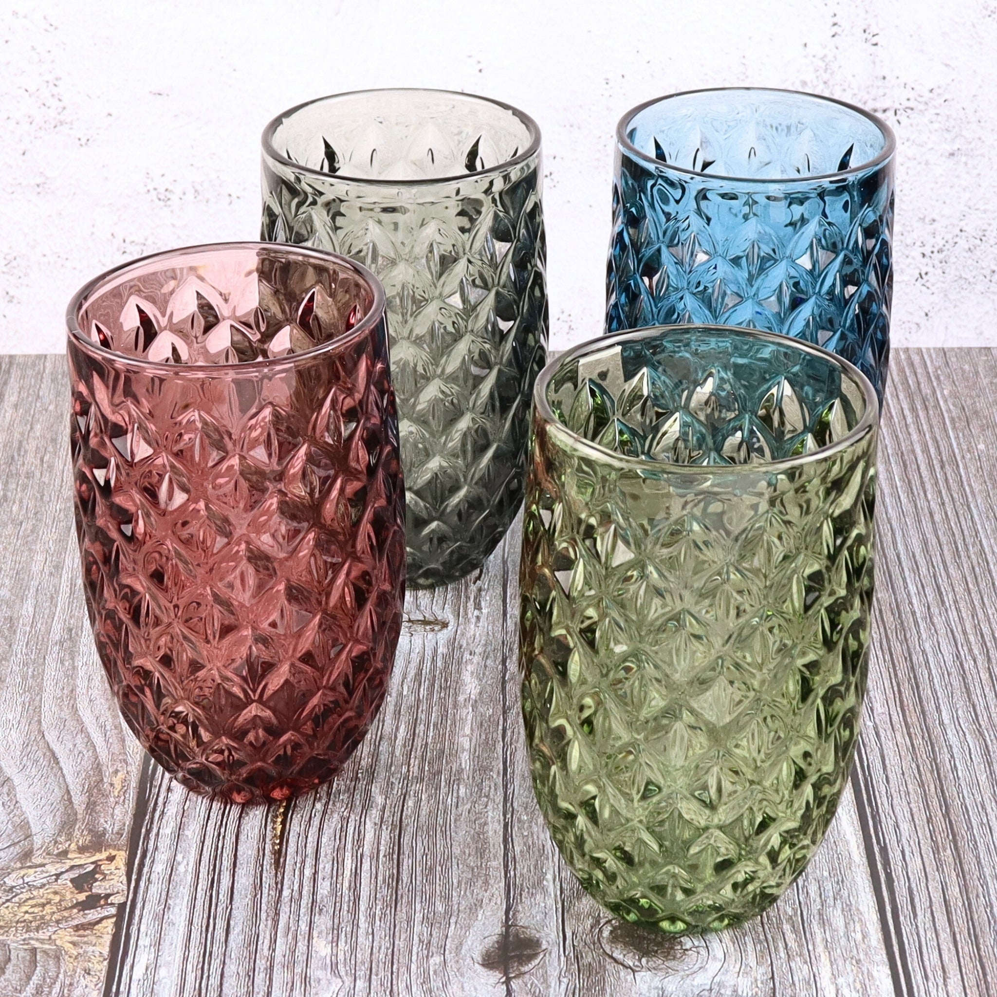 Four textured glass tumblers in pink, green, blue, and clear on a wooden surface.