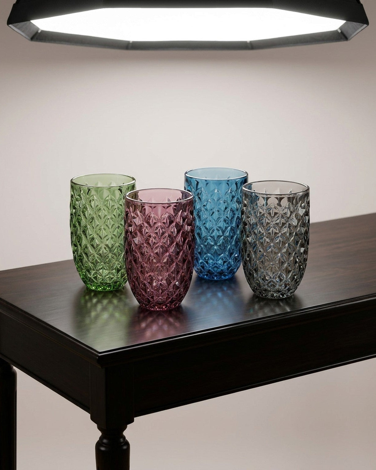 Four textured glass tumblers in pink, green, blue, and green on a wooden surface.