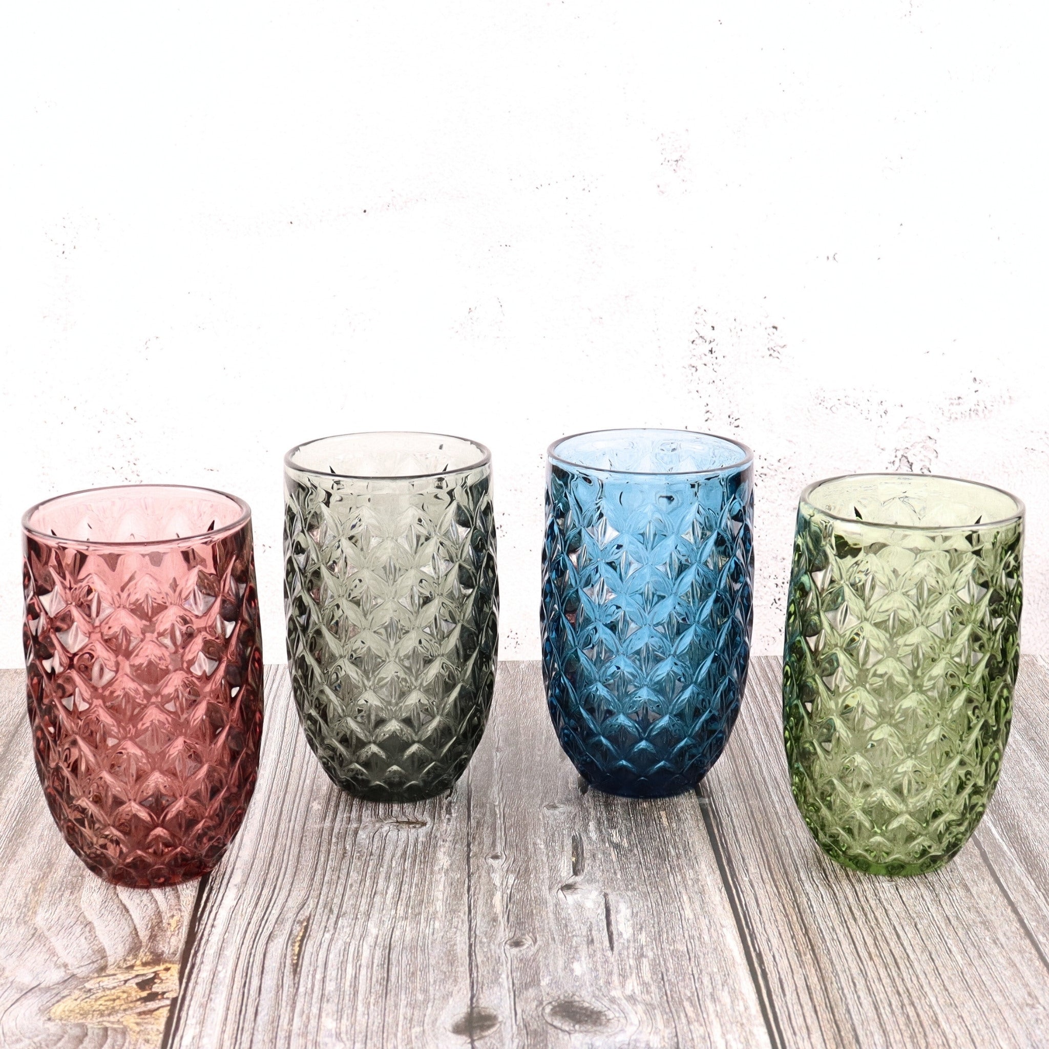 Four textured glass tumblers in pink, green, blue, and green on a wooden surface.