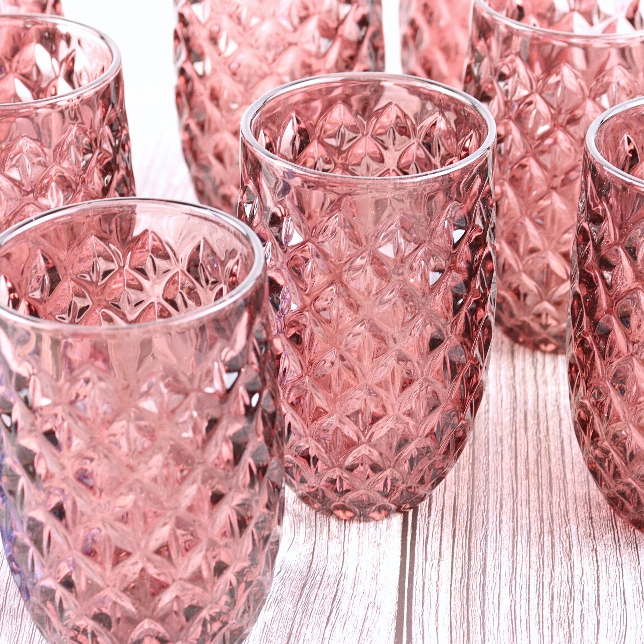 Set of pink glass tumblers with textured design on a wooden surface