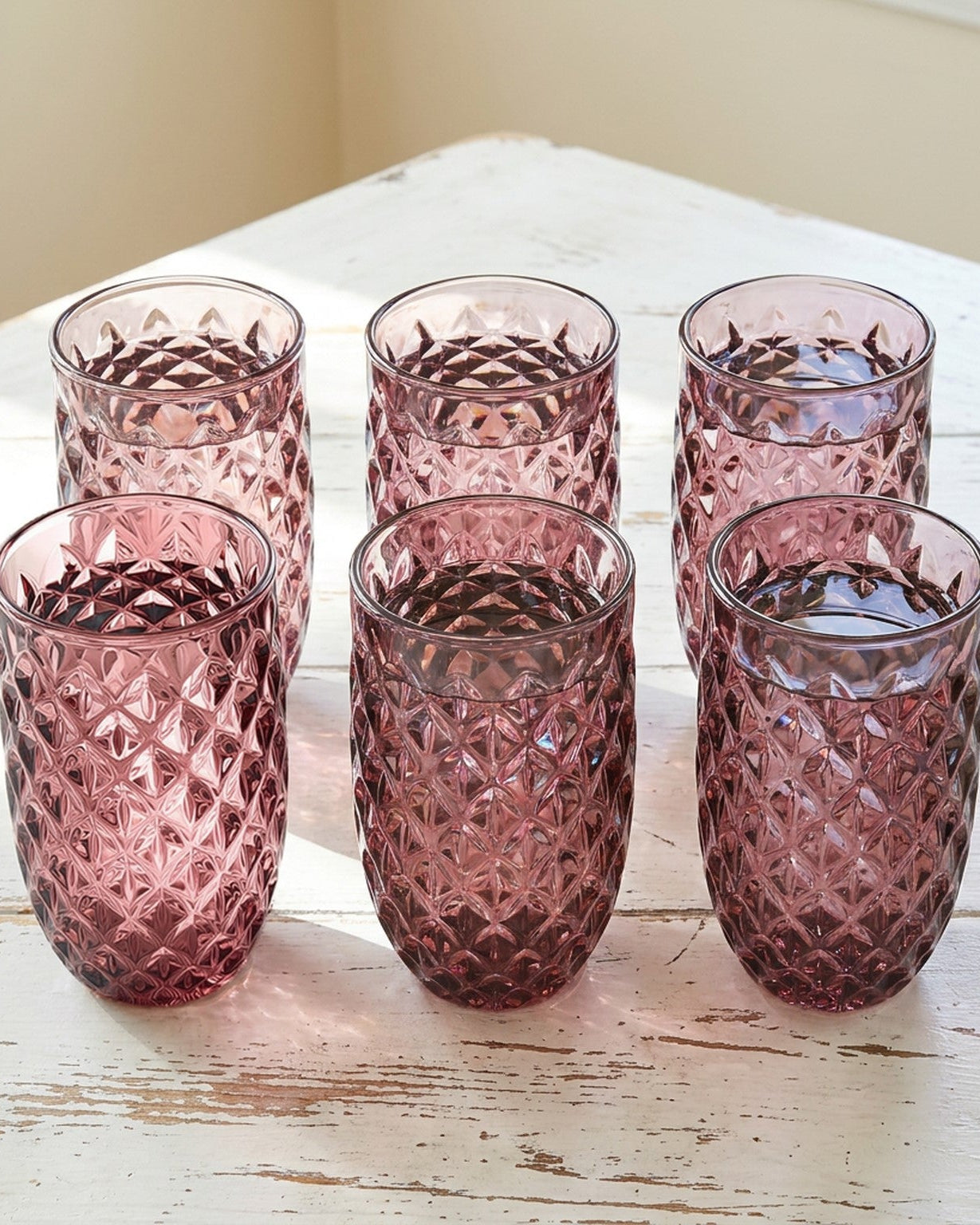 Set of pink textured glass tumblers with a blue candle holder on a wooden surface