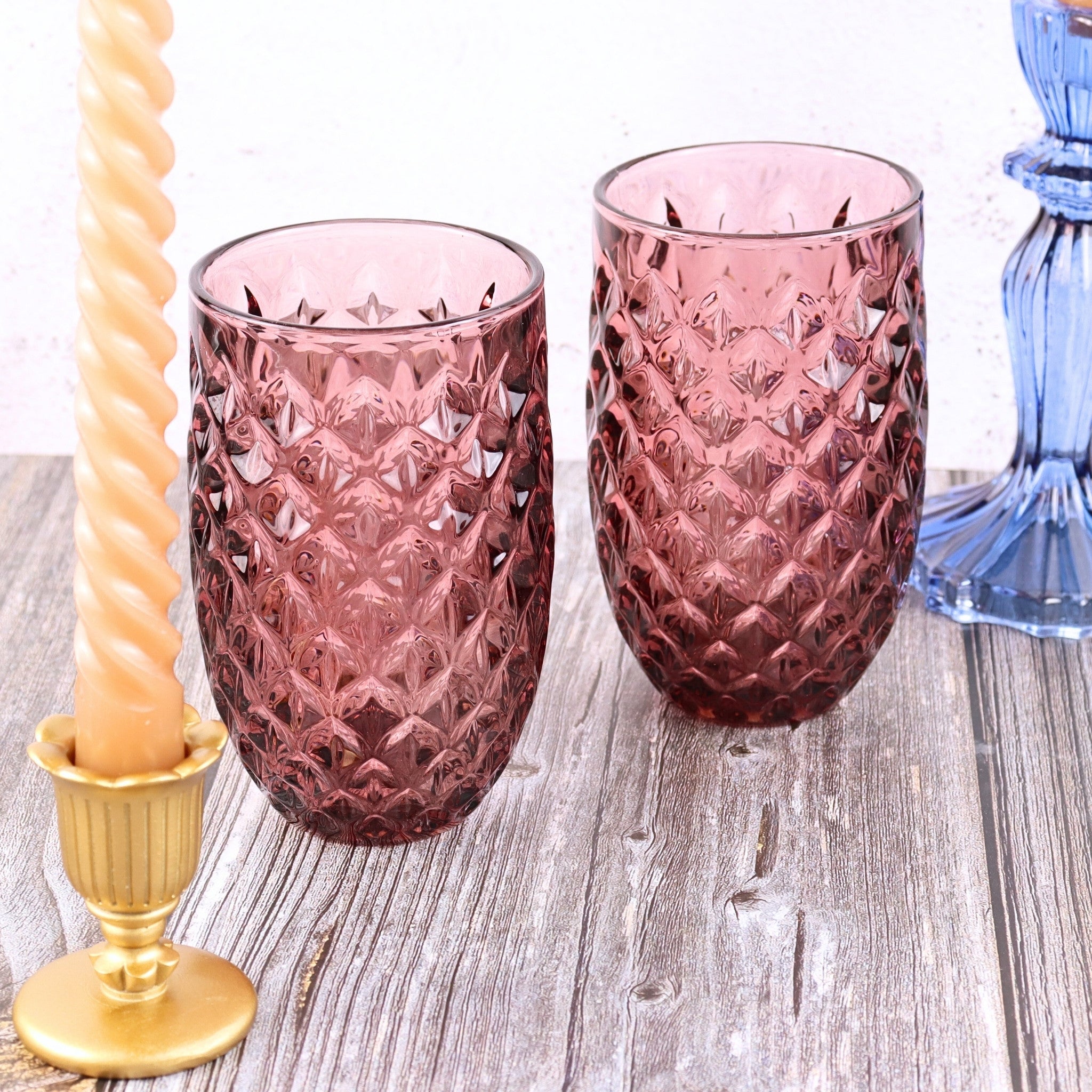 Two pink textured glass tumblers on a wooden surface with decorative elements.