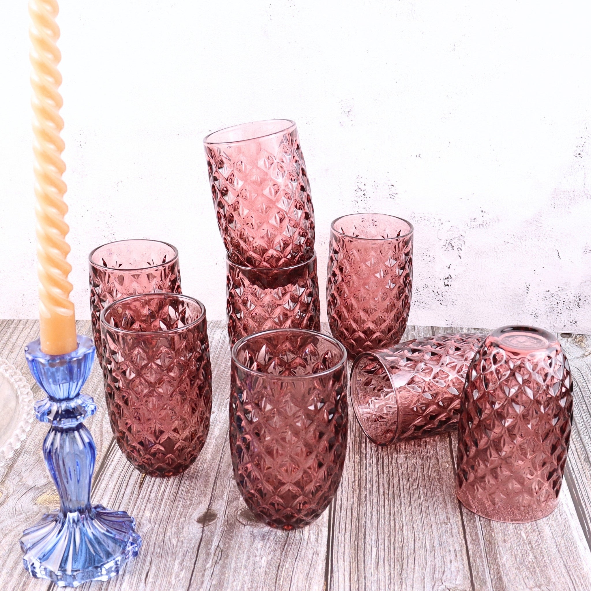 Set of pink textured glass tumblers on a wooden surface with a blue candle holder.