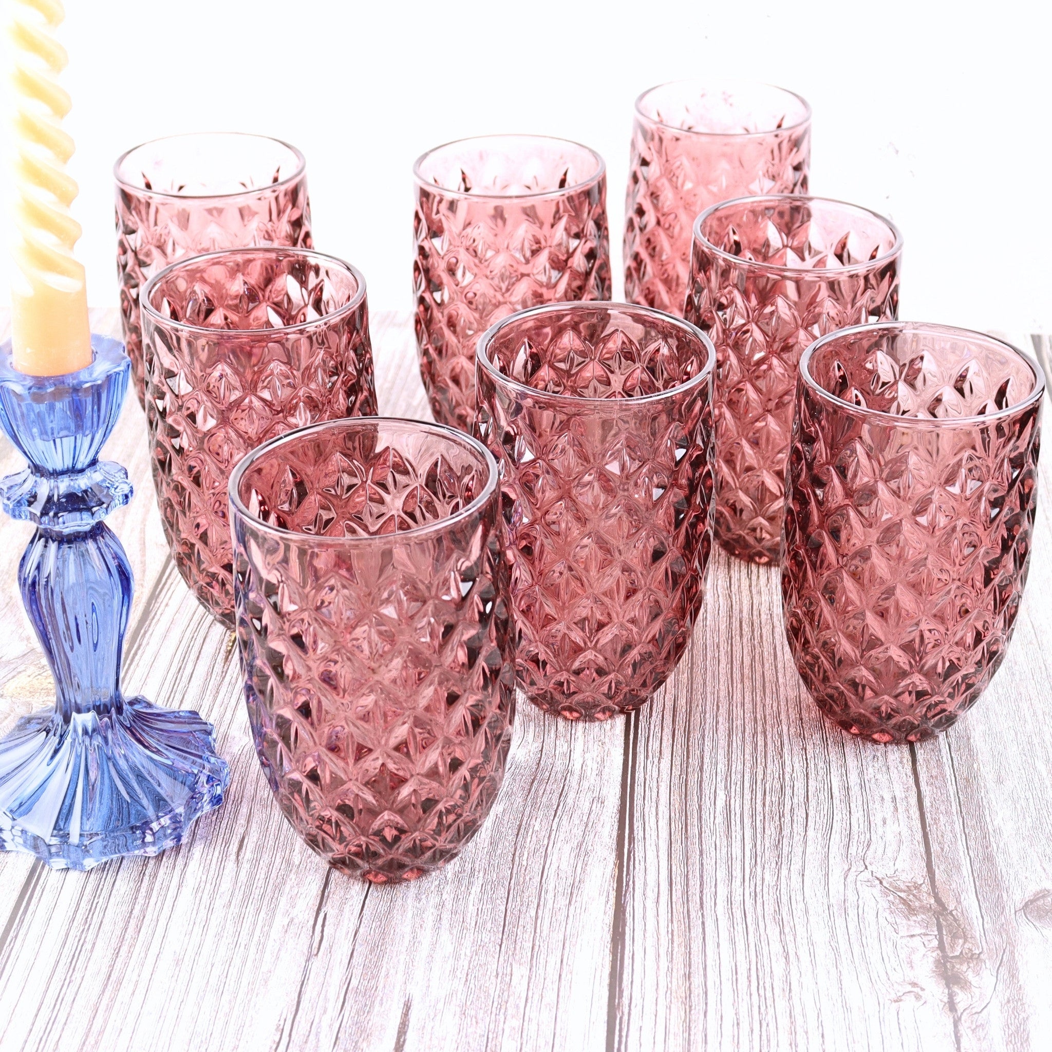 Set of pink glass tumblers on a wooden surface with a blue candle holder.