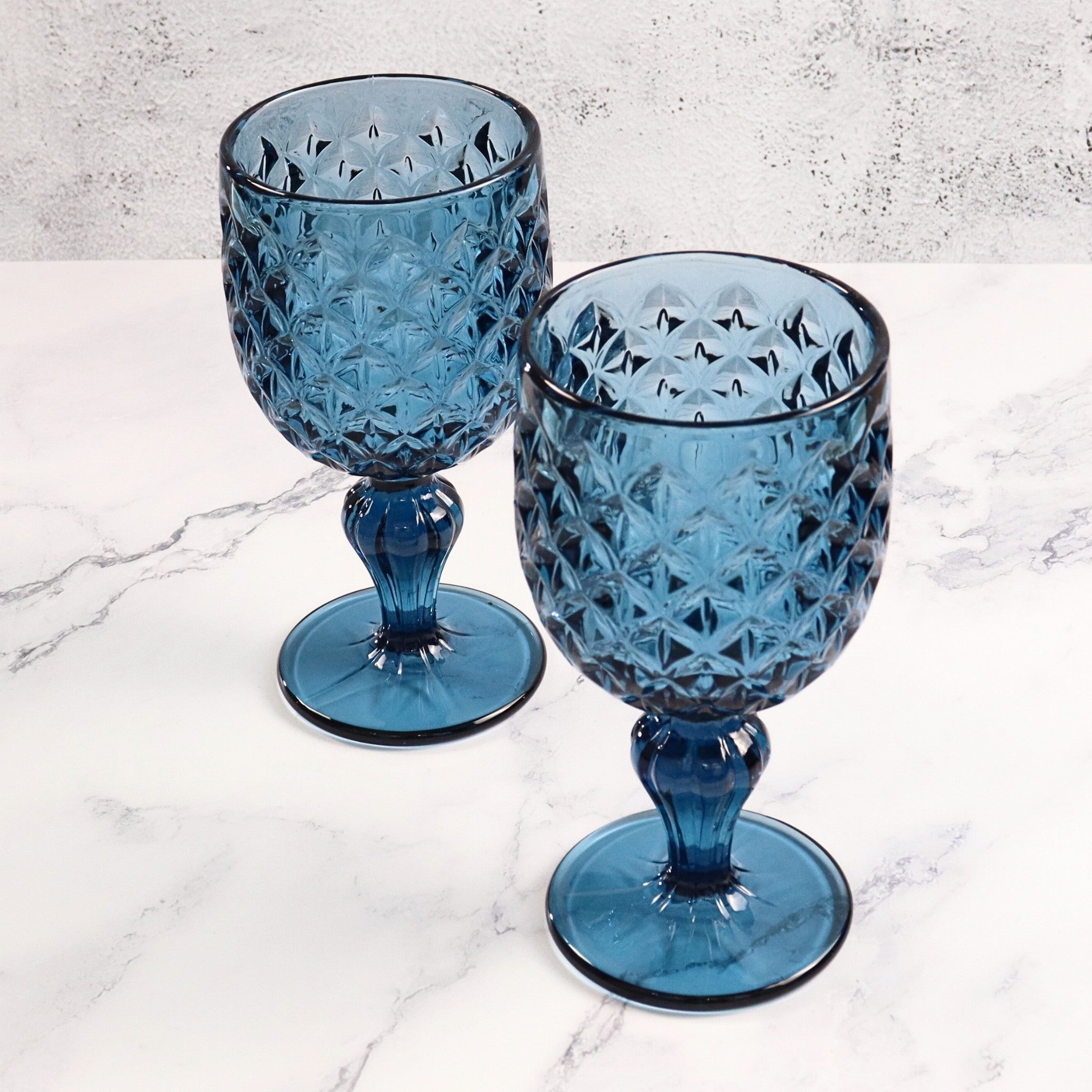 Two blue glass goblets with diamond pattern on a marble surface